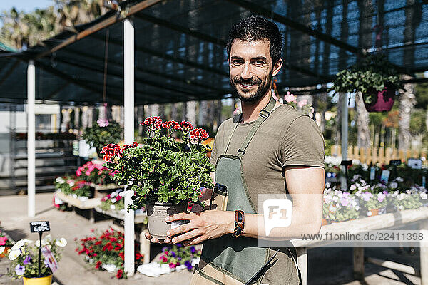 Portrait of a smiling gardener in a garden center holding flower