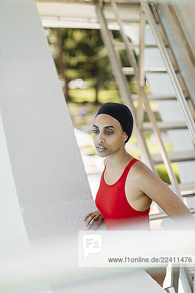 Portrait of young woman wearing swimming cap and red bathsuit standing on stairs of highboard