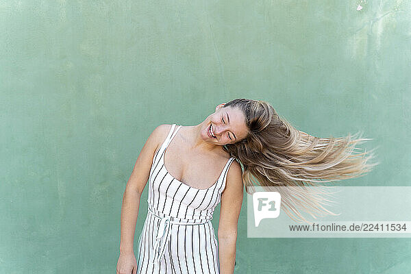 Blond young woman tossing her hair in front of green wall