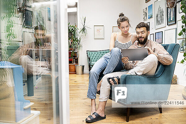 Young couple sitting in arm chair  using digital tablet