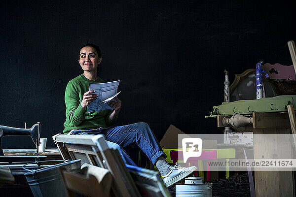 Creative small business owner in a workshop holding papers and smiling