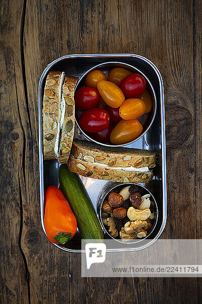 Lunchbox with pumpkin seed bread  cucumber  bell pepper  tomatoes and nuts