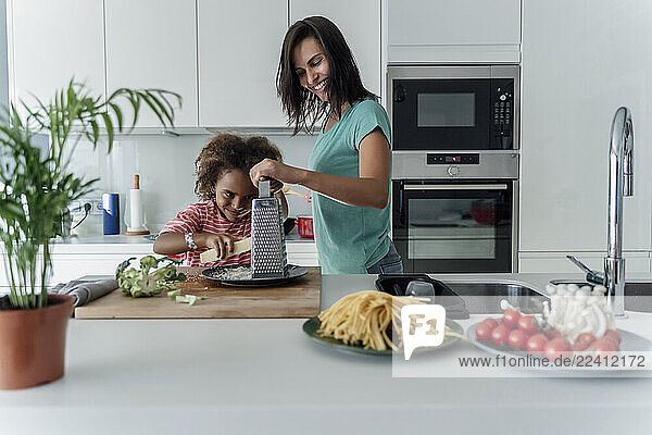 Mother and daughter cooking in kitchen together grating cheese