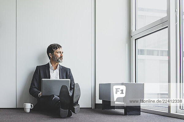 Mature businessman in office sitting on the floor with laptop