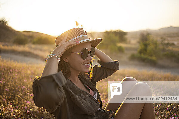Young woman sitting on meadow at sunset