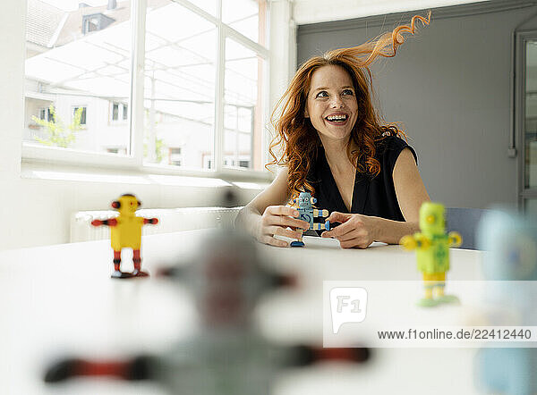 Portrait of redheaded woman in a loft with miniature robots on desk
