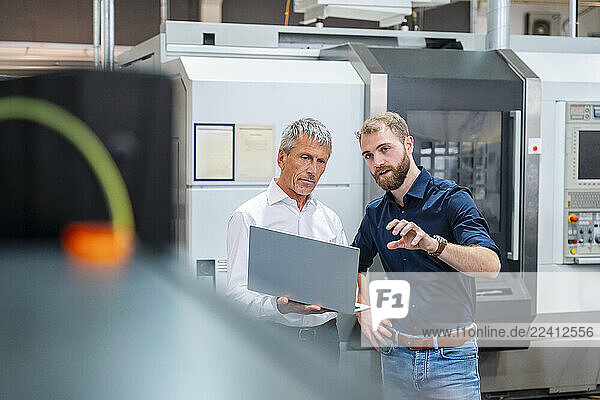 Two men discussing in a production hall with a laptop and machine system