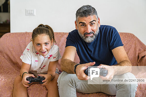 Father and daughter playing video game on couch at home