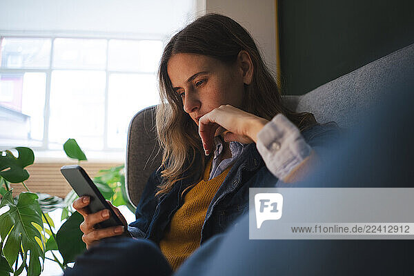 Young woman sitting on a couch using a smartphone indoors