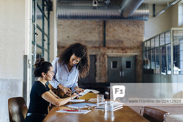 Two young businesswomen talking at conference table in loft office