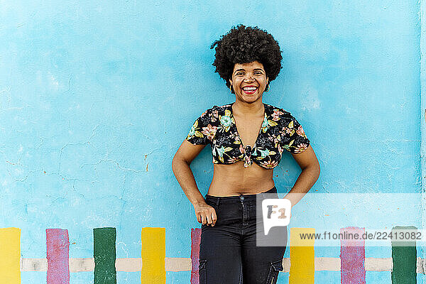 Smiling Afro-American woman in front of a blue wall looking at camera