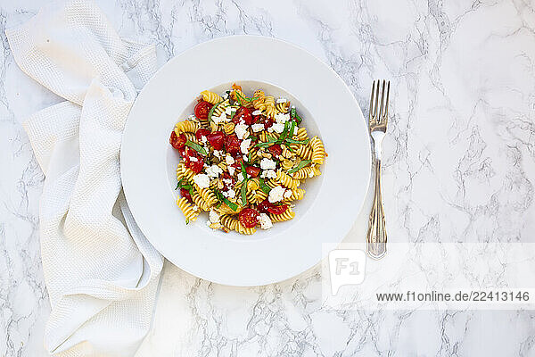 Fusilli pasta with tomatoes  feta cheese  and pine nuts on a marble background
