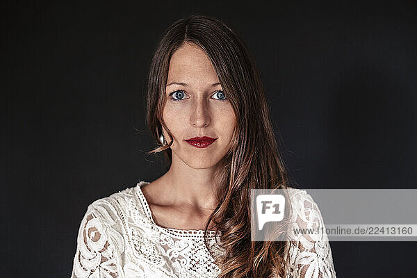 Portrait of young woman with reed lips  blue eyes and long brown hair against black background