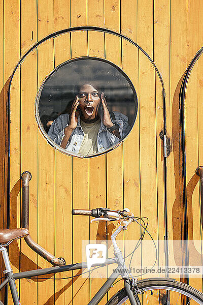 Young man behind wooden door  looking amazed through round window