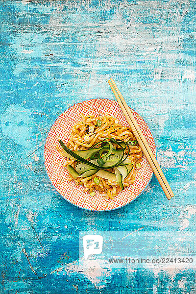 Udon noodles with peanut butter sauce and vegetables on a plate with chopsticks on a blue background