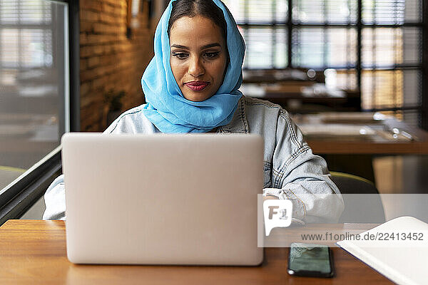 Businesswoman wearing turquoise hijab in a cafe and working  using laptop