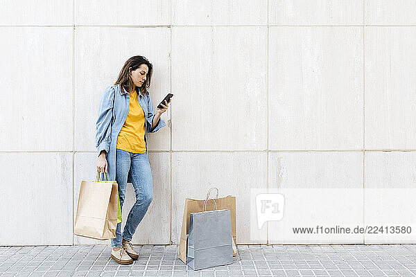 Young brunette woman using smartphone after shopping
