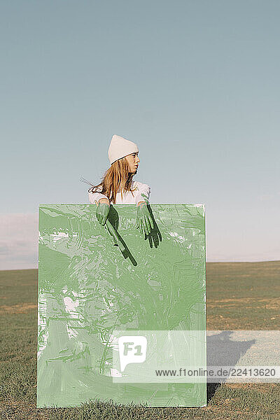 Young woman holding green painting on dry field