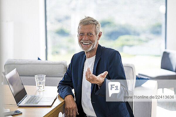 Portrait of smiling senior businessman with laptop sitting at desk at home