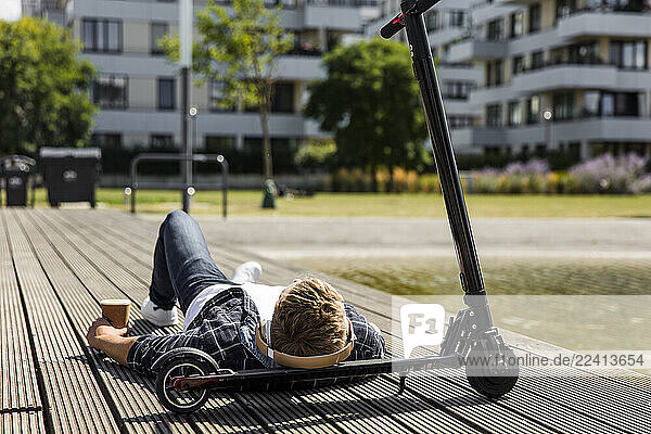 Young man with e-scooter lying on boardwalk