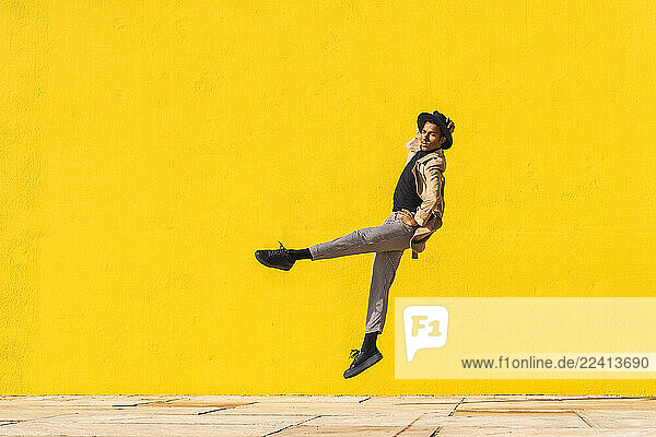 Young man dancing in front of yellow wall  jumping mid air