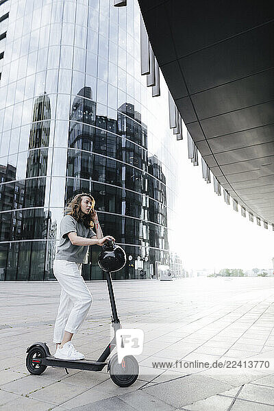 Woman with e-scooter and helmet  modern office buildings in the background