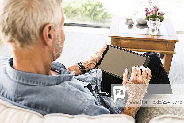 Senior man using tablet on couch at home