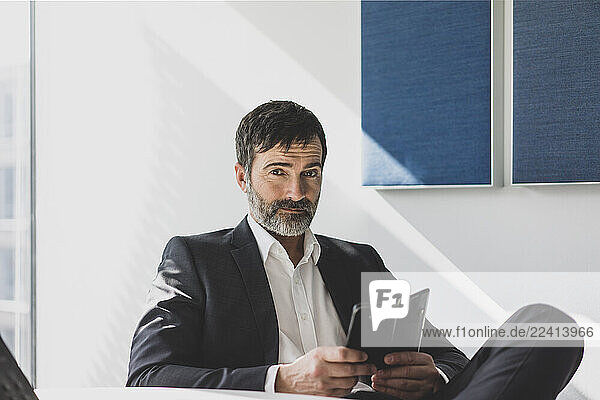 Portrait of confident mature businessman with cell phone in office