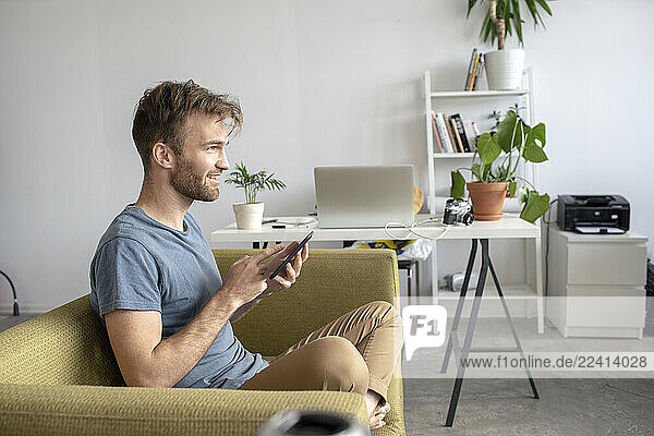 Smiling man sitting on couch in office using tablet