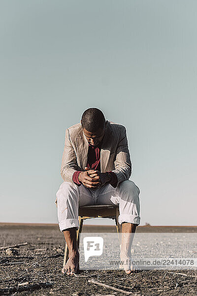 Pensive young man sitting on chair in barren land