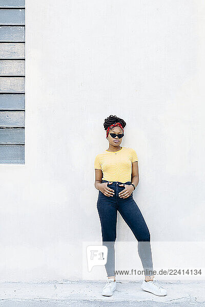 Young woman wearing hair-band and sunglasses leaning against white wall