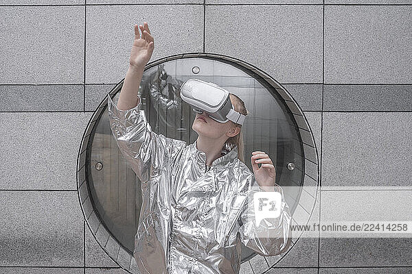 Girl in silver suit looking through VR goggles  watching her hand