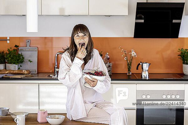Portrait of woman wearing pyjama eating fruit in kitchen at home