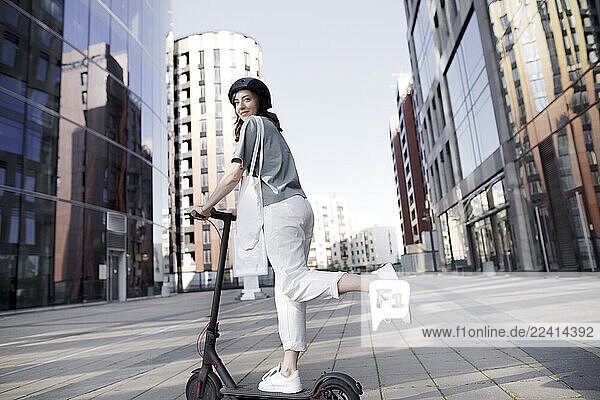 Woman with e-scooter and helmet  modern office buildings in the background