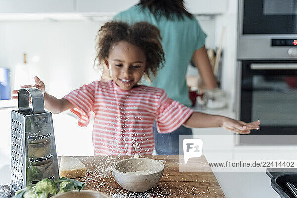 Girl playing with grated cheese in kitchen