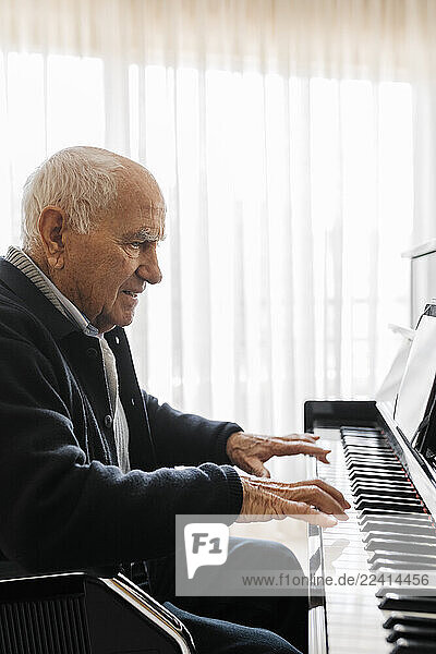 Senior man sitting in wheelchair playing piano at home
