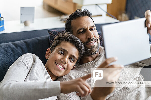 Happy father and son using tablet on couch in living room
