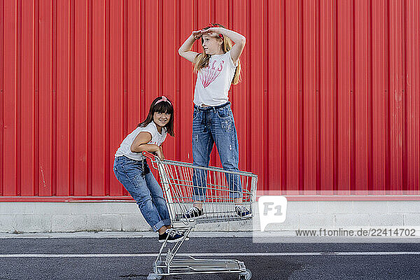 Sisters with shopping cart in front of red wall