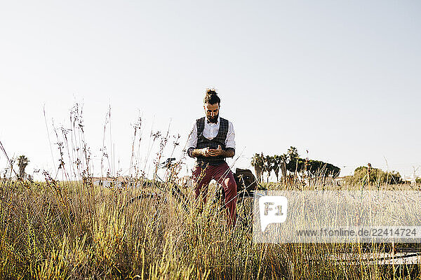 Well dressed man with his bike on a wooden walkway in the countryside using cell phone