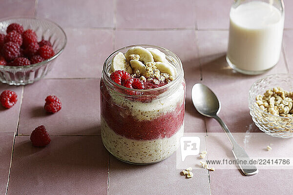 Vegan raspberry-banana overnight oats in a glass jar with oat milk in a studio setting