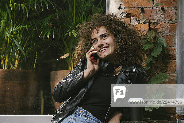 Portrait of happy teenage girl on the phone sitting at outdoor cafe with coffee to go
