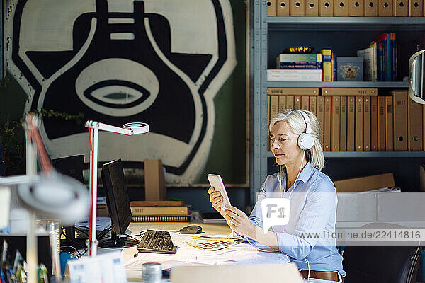 Mature woman talking on the phone with headphones  sitting in architect s office
