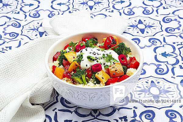 Bowl of couscous with grilled vegetables and yoghurt sauce on a patterned tablecloth