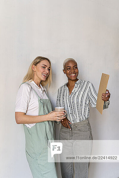 Two smiling women with clipboard and cup of coffee