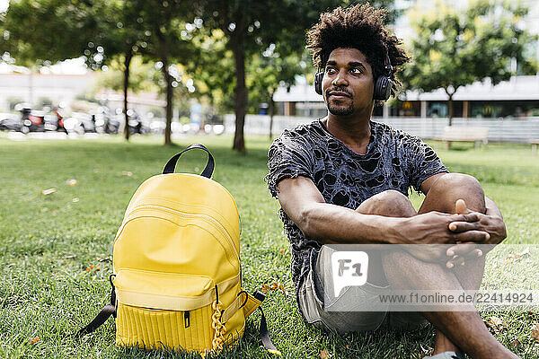 Portrait of man sitting on a meadow listening music with cordless headphones  Barcelona  Spain