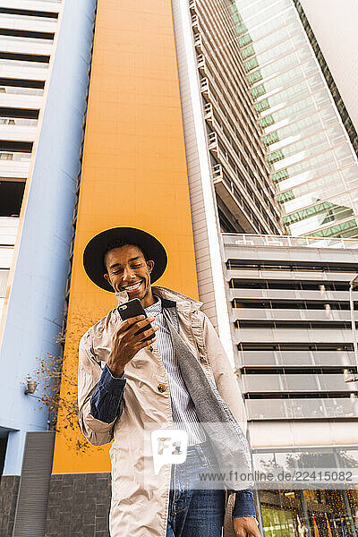 Smiling fashionable young man using smartphone outdoors