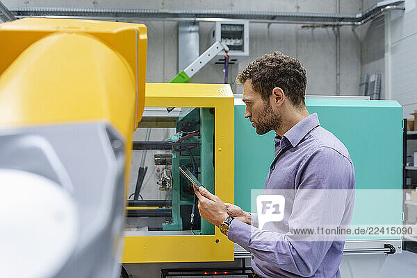 Man using tablet in industrial production hall with robot
