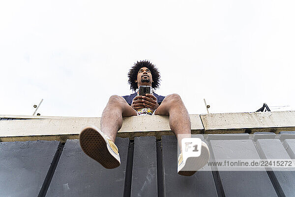 Low angle view of stylish man with cell phone sitting on a wall