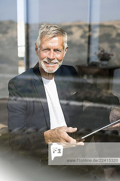 Smiling senior businessman using tablet at the window