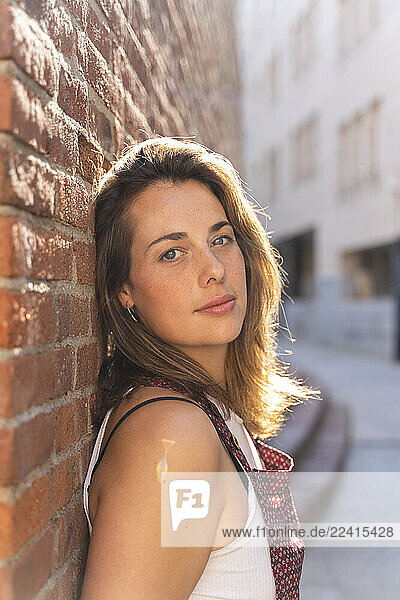 Young woman leaning on brick wall and looking at camera